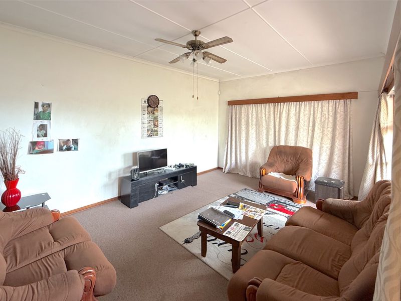 A living room featuring a ceiling fan, carpeted flooring, and curtain rails, presenting a dated aesthetic that would benefit from modernization.