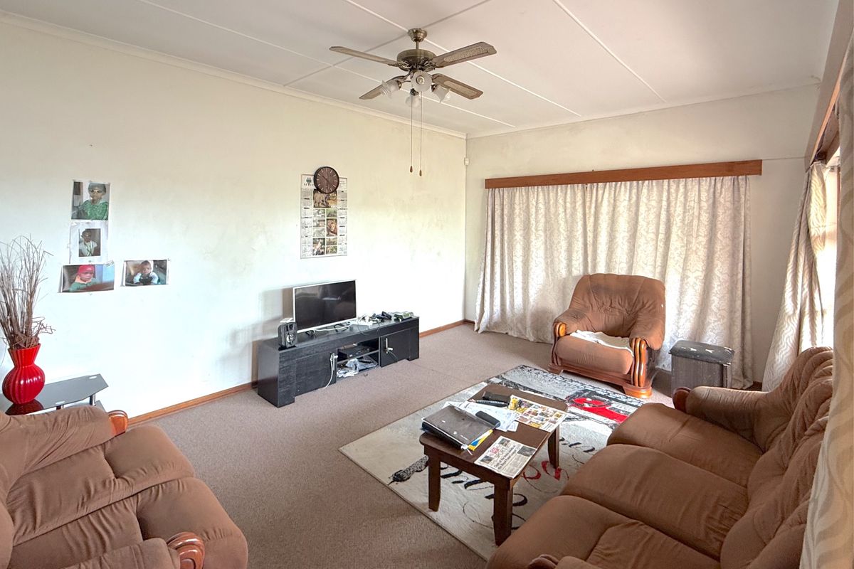 A living room featuring a ceiling fan, carpeted flooring, and curtain rails, presenting a dated aesthetic that would benefit from modernization.