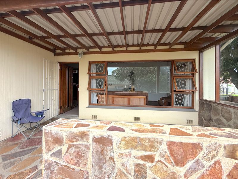 A covered outdoor patio area featuring a timber pergola, stone-clad wall, and stone flooring, providing a functional space for outdoor relaxation.