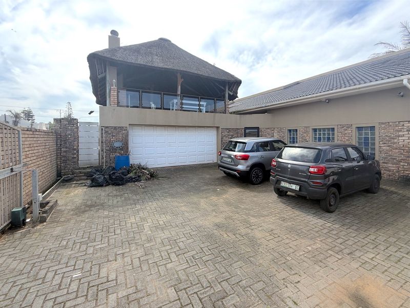 Front exterior view featuring a paved driveway, garage access, and an elevated thatched-roof patio area with glass balustrades.