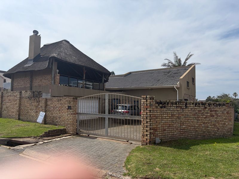 Front exterior view of a house featuring a combination of thatched and tiled roofing, enclosed by a brick boundary wall with a metal gate.