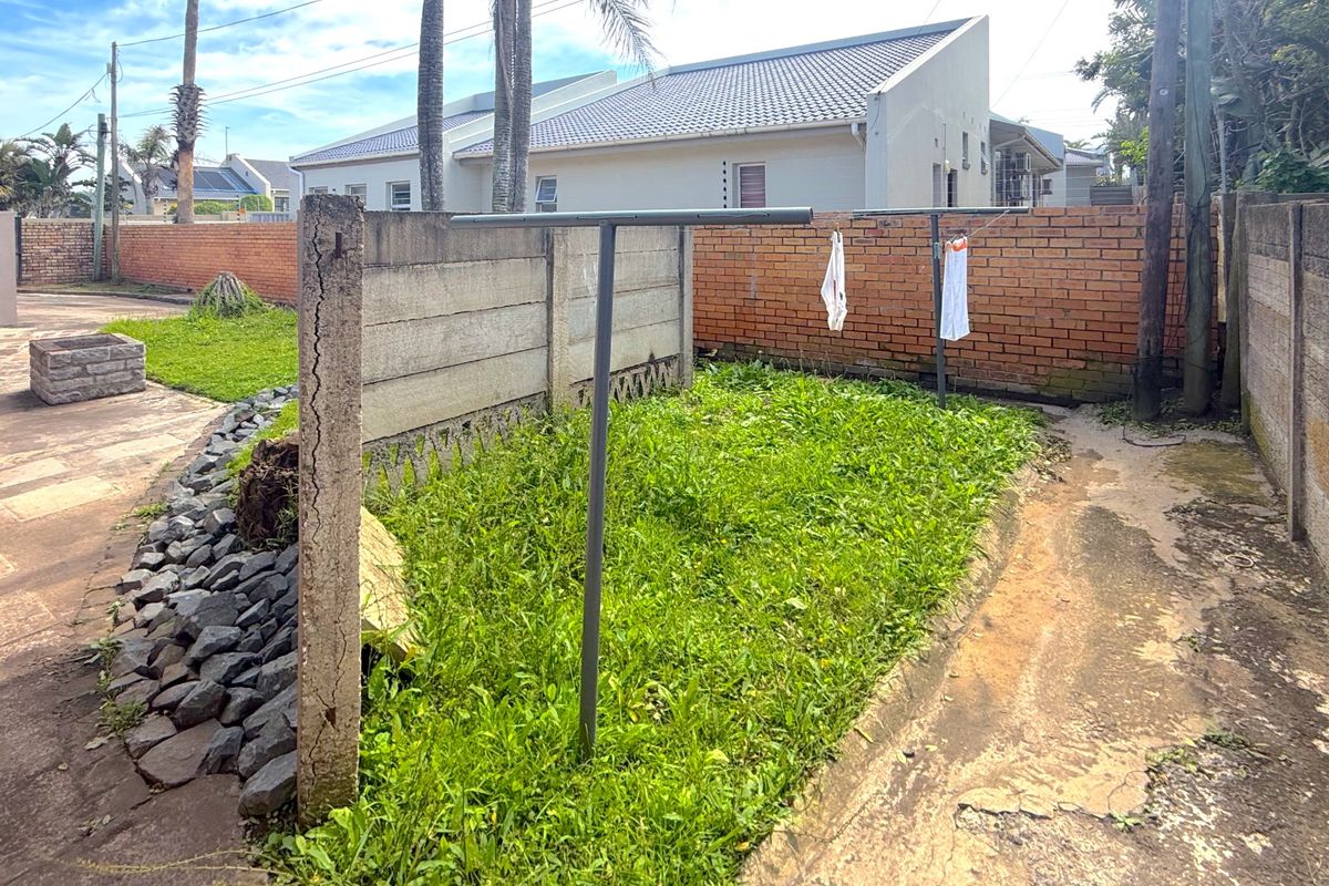 Rear exterior area featuring a brick and precast concrete boundary wall, concrete paving, and a metal washing line in a garden space.