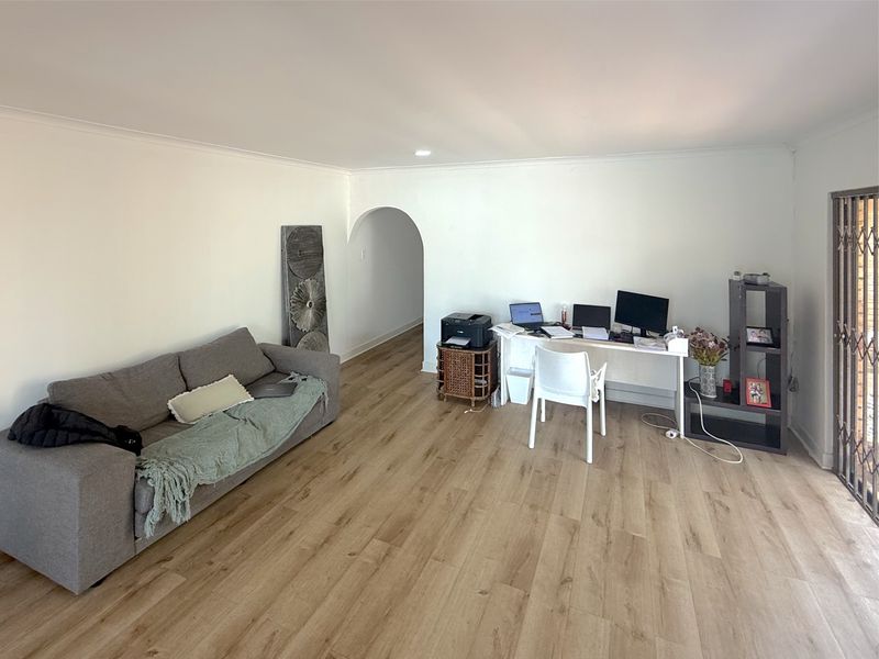 A spacious living area featuring light-toned laminate flooring, neutral walls, and an arched entryway leading to adjacent rooms.