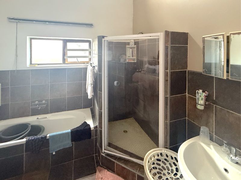 A functional bathroom featuring a built-in bathtub, separate shower enclosure, and pedestal basin with dark tiled wall finishes.