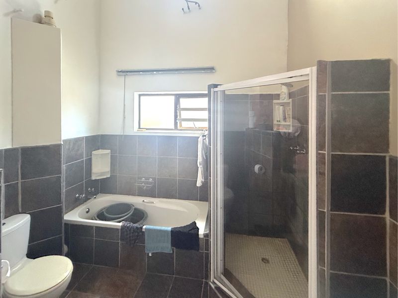 A functional bathroom featuring a built-in bathtub, separate shower enclosure, and tiled finishes throughout, offering a practical layout for daily use.