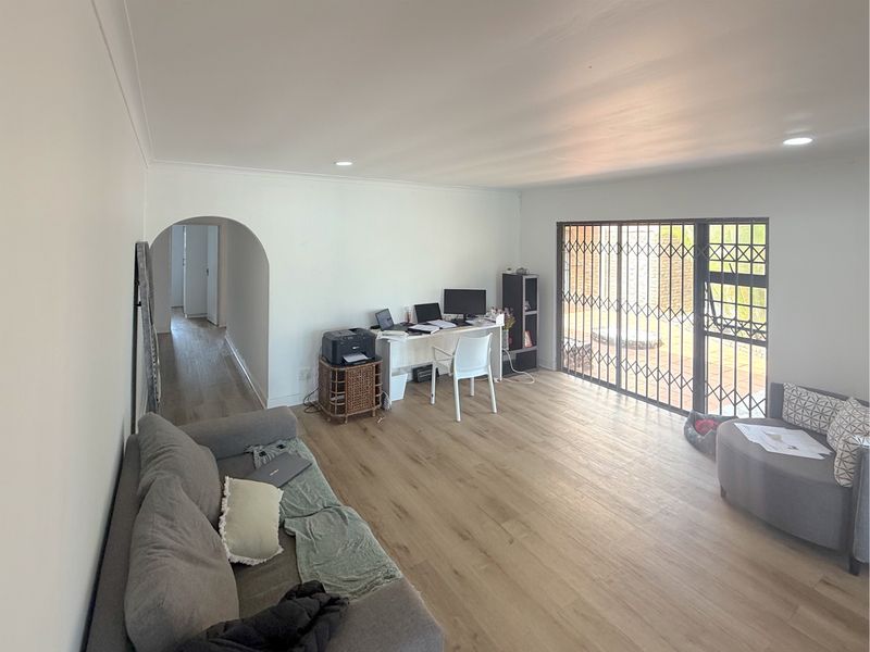 Spacious living room featuring light-toned laminate flooring, recessed lighting, and a large sliding glass door with a security gate leading to the exterior.
