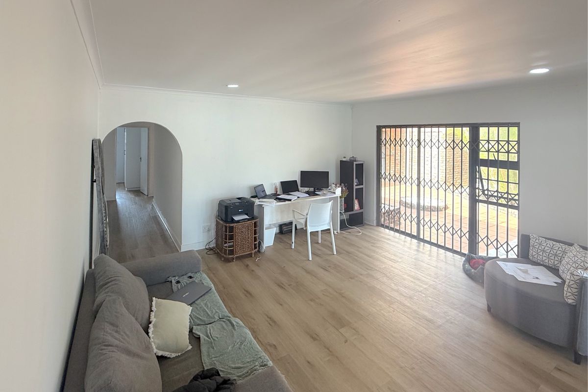 Spacious living room featuring light-toned laminate flooring, recessed lighting, and a large sliding glass door with a security gate leading to the exterior.