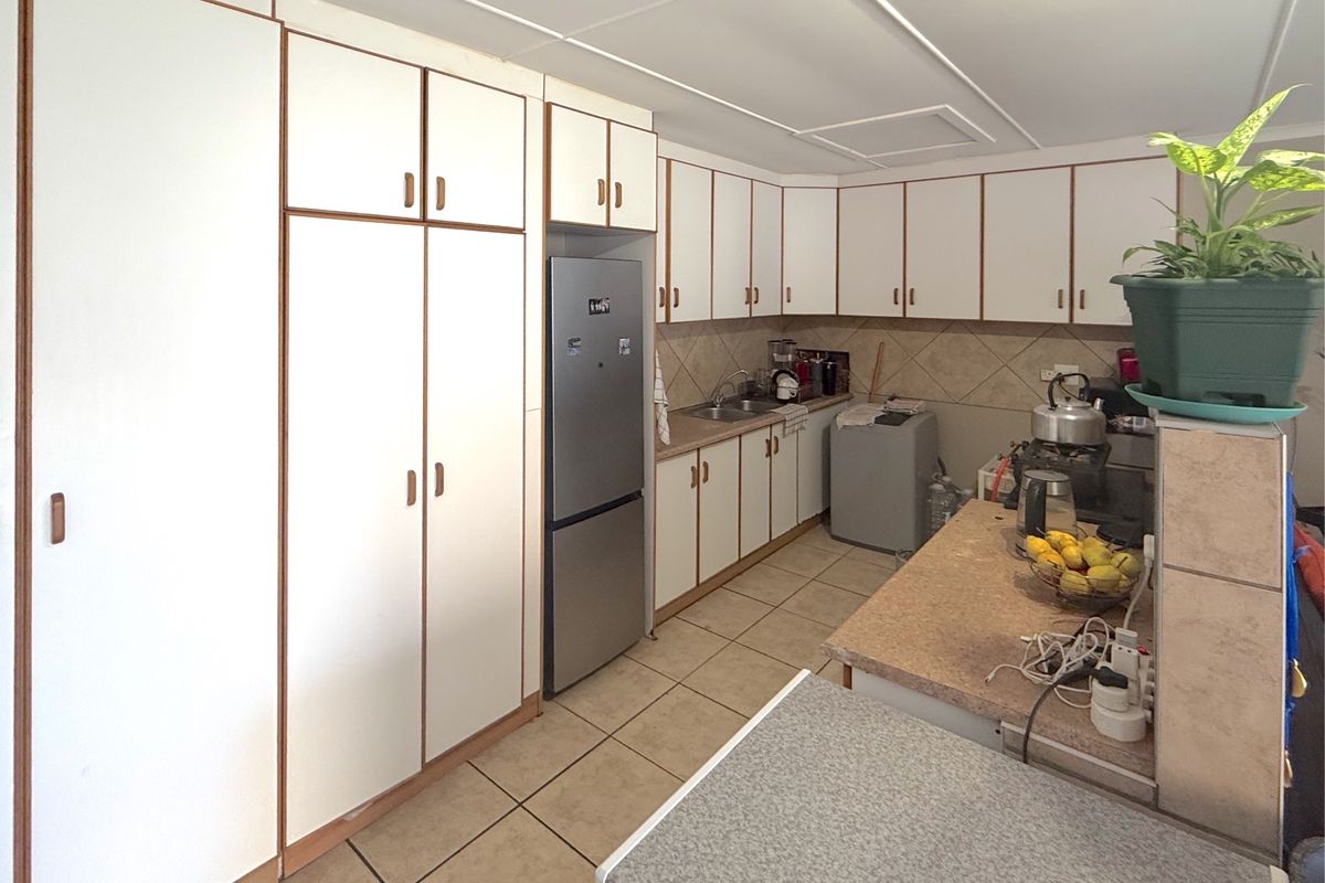 A functional kitchen featuring extensive built-in cabinetry, laminate countertops, tiled backsplash, and tiled flooring, offering a practical layout for daily use.