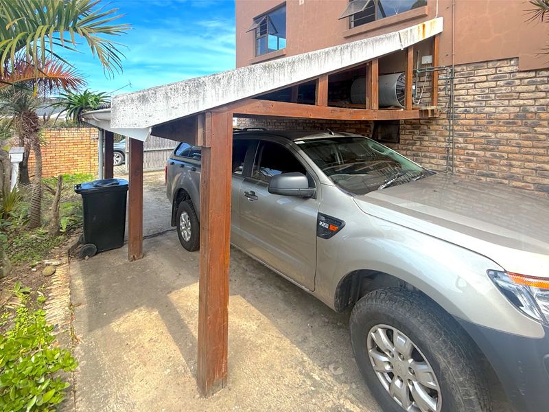 An outdoor timber carport structure attached to the side of the house, featuring an exposed geyser unit and concrete driveway surface.