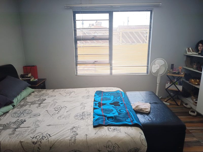A functional bedroom featuring laminate flooring and a large window with fitted venetian blinds, providing natural light.