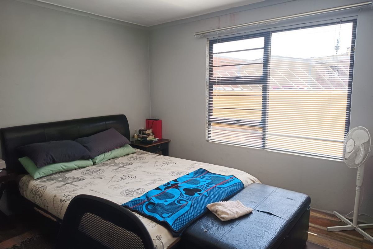 A functional bedroom featuring laminate flooring, neutral wall finishes, and a large window with horizontal blinds providing natural light.