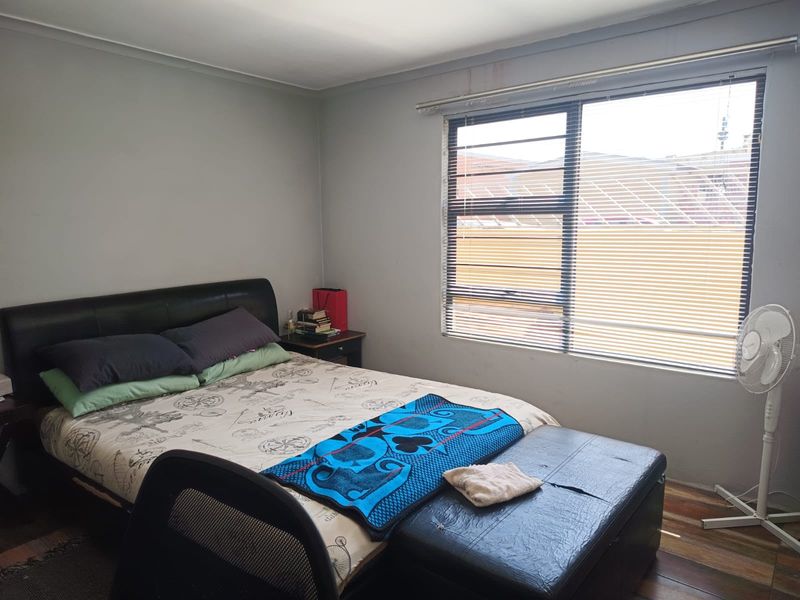 A functional bedroom featuring laminate flooring, neutral wall finishes, and a large window with horizontal blinds providing natural light.