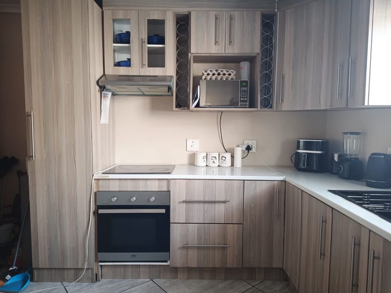A functional kitchen featuring wood-look cabinetry, built-in oven, electric hob, extractor fan, and tiled flooring.