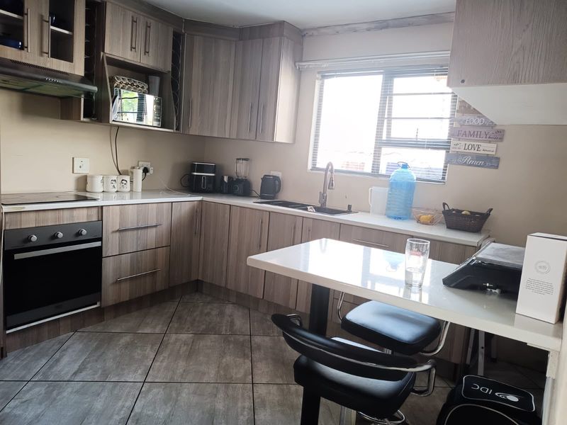 A functional kitchen featuring wood-look cabinetry, laminate countertops, built-in oven, extractor fan, and tiled flooring with a breakfast nook area.