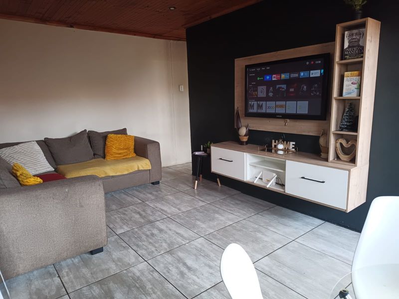 A living room featuring tiled flooring, a timber-clad ceiling, and a modern built-in media unit against a dark accent wall.