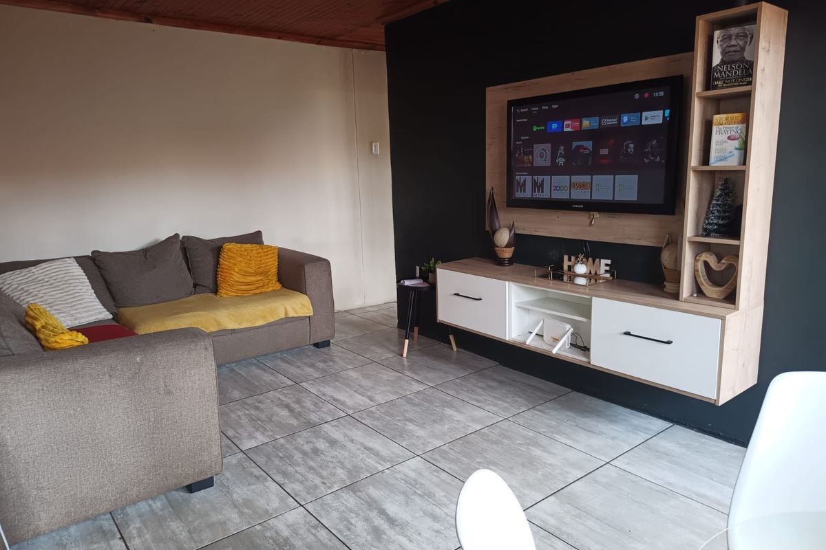 A living room featuring tiled flooring, a timber-clad ceiling, and a modern built-in media unit against a dark accent wall.