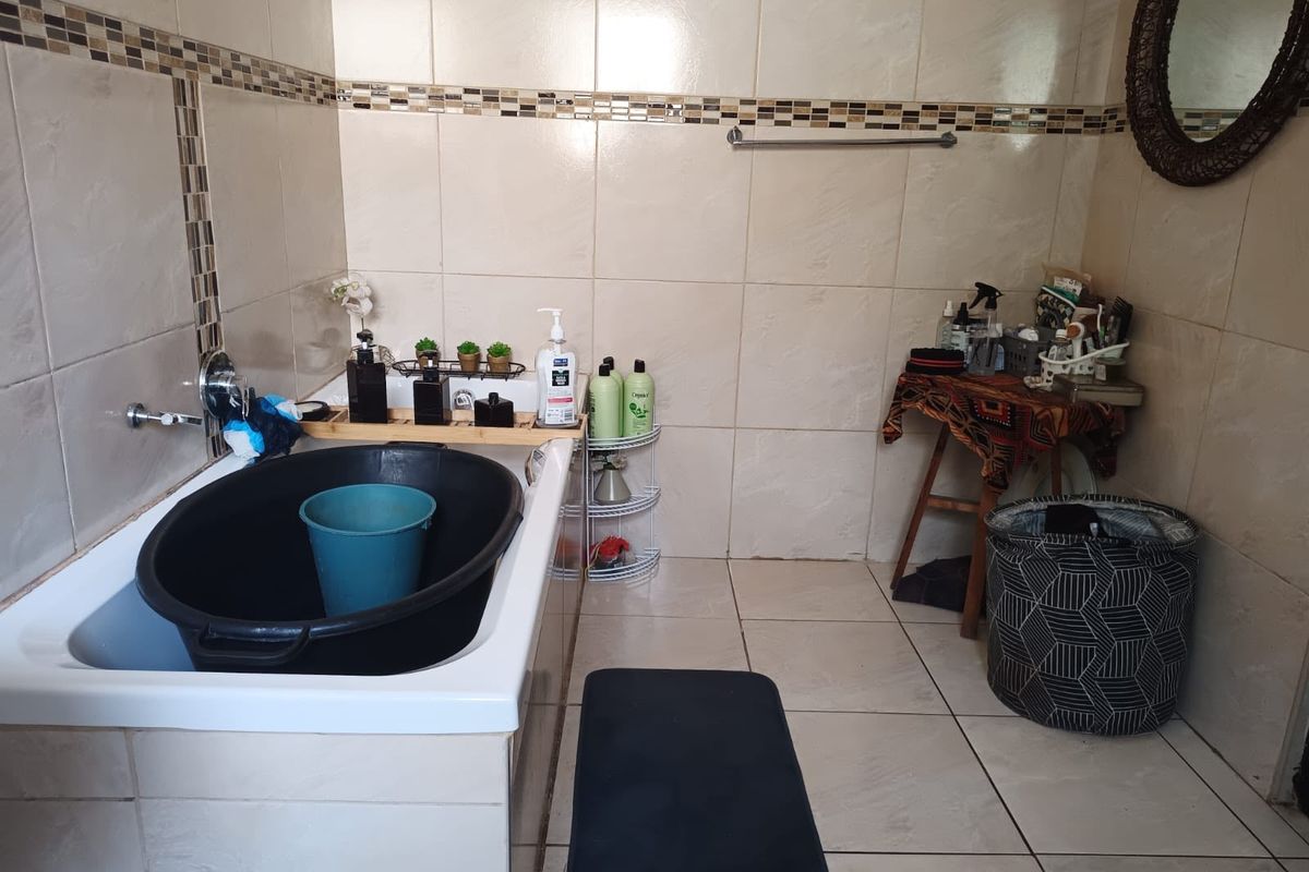 A functional bathroom featuring full-height wall tiling, floor tiles, and a built-in bathtub with a wall-mounted mixer tap.