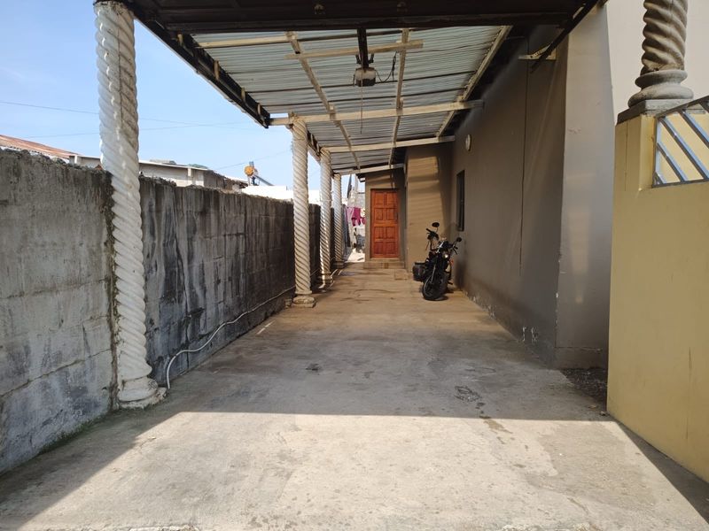 A covered outdoor patio area featuring decorative spiral columns, a concrete boundary wall, and a corrugated metal roof structure.