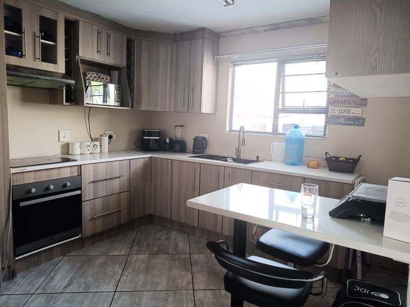 A functional kitchen featuring wood-look cabinetry, laminate countertops, built-in oven and hob, and tiled flooring with a window providing natural light.