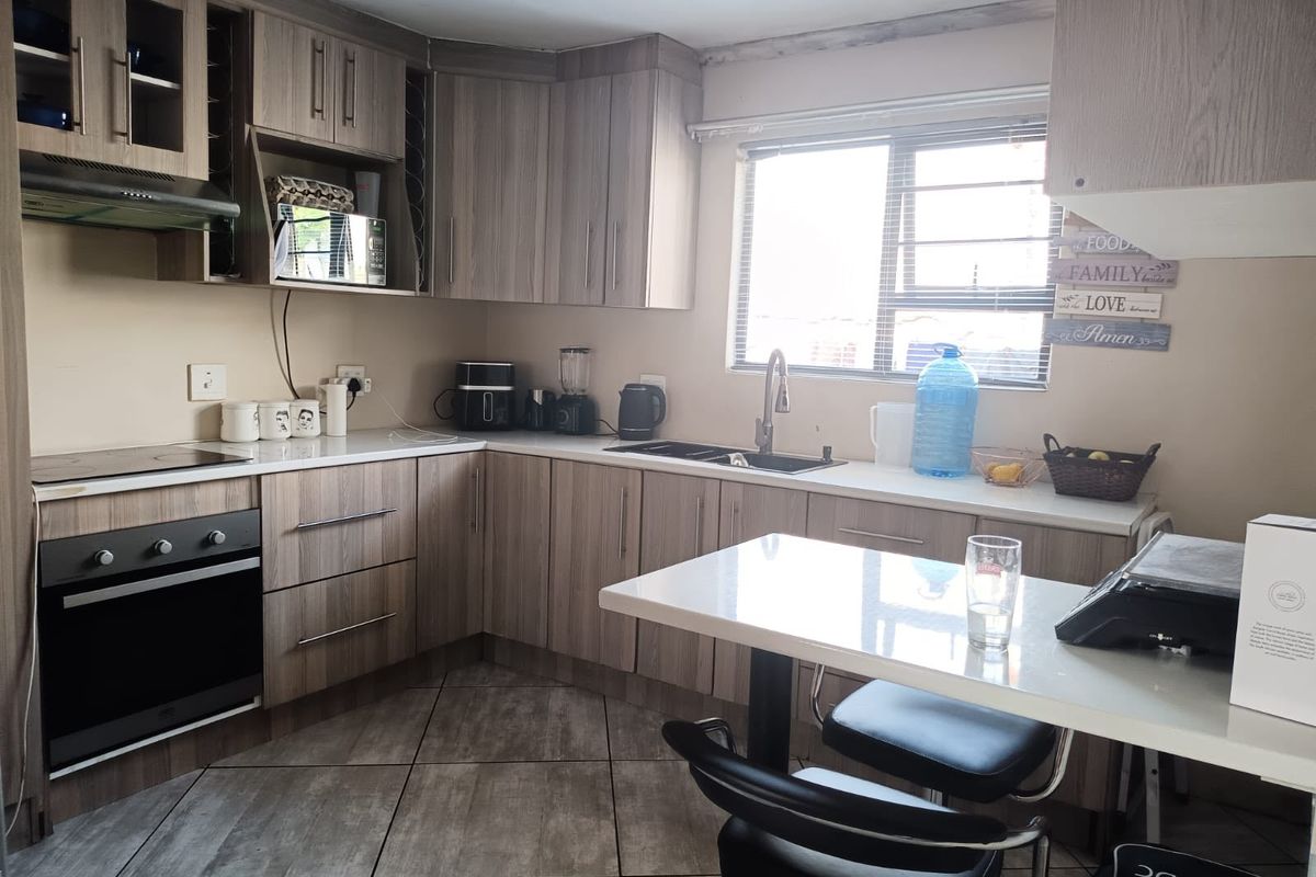 A functional kitchen featuring wood-look cabinetry, laminate countertops, built-in oven and hob, and tiled flooring with a window providing natural light.