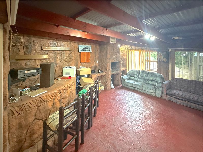Rustic entertainment area featuring a built-in bar, stone-clad walls, a built-in braai, and exposed timber ceiling beams.