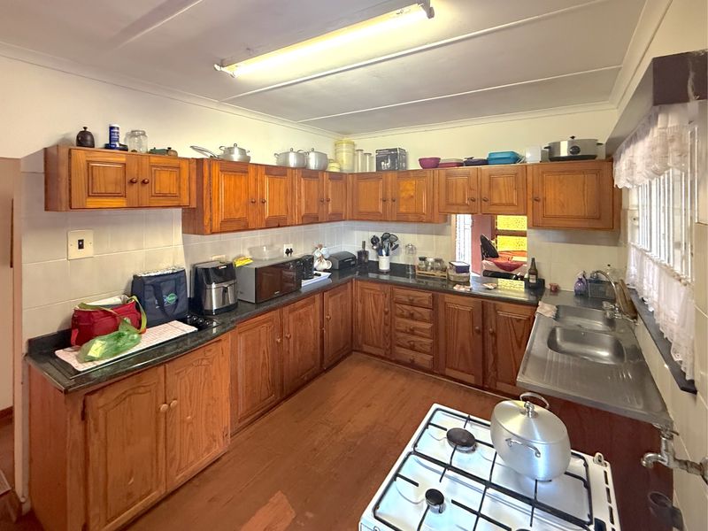 A functional kitchen featuring traditional wooden cabinetry, a double bowl stainless steel sink, gas hob, and tiled splashbacks, offering potential for modern updates.