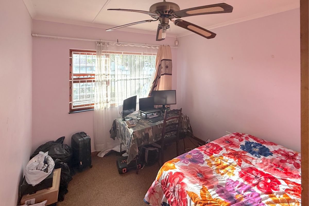 A bedroom featuring a ceiling fan, carpeted flooring, and window security bars, requiring cosmetic updates to improve its overall appeal.