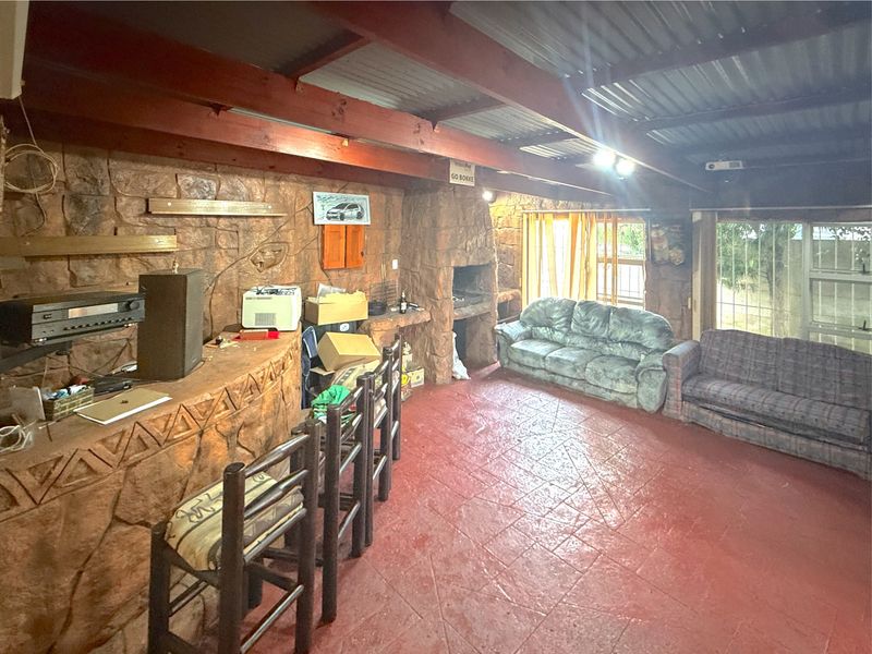 Rustic entertainment area featuring a built-in stone bar, stone fireplace, exposed timber beams, and tiled flooring.