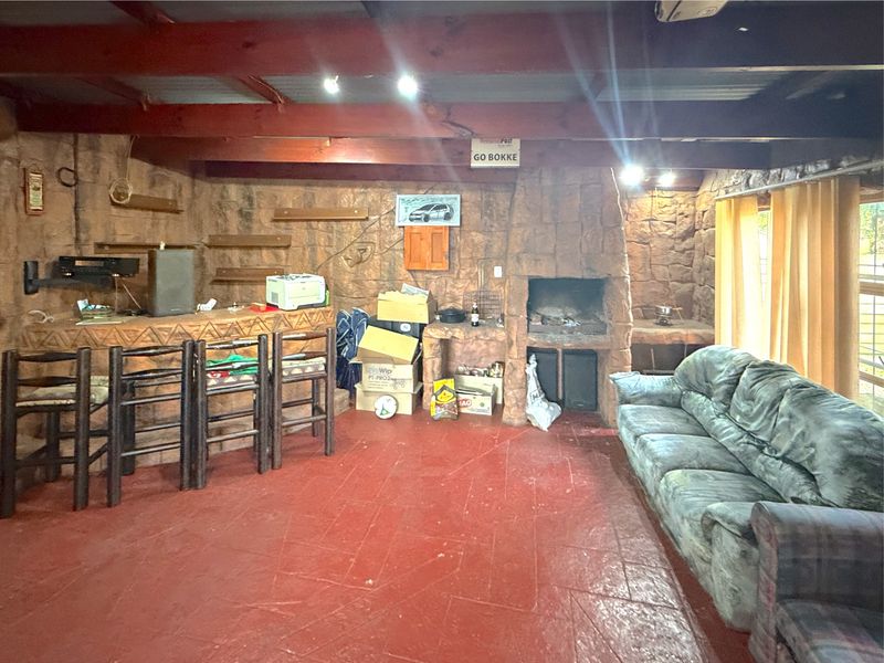 Rustic living area featuring a built-in stone fireplace, stone bar counter, and exposed timber ceiling beams with painted concrete flooring.