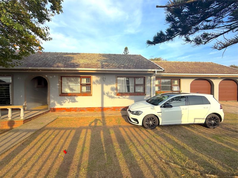 Front elevation of a single-story house featuring a tiled roof, brick plinth detailing, security bars on windows, and a double garage.