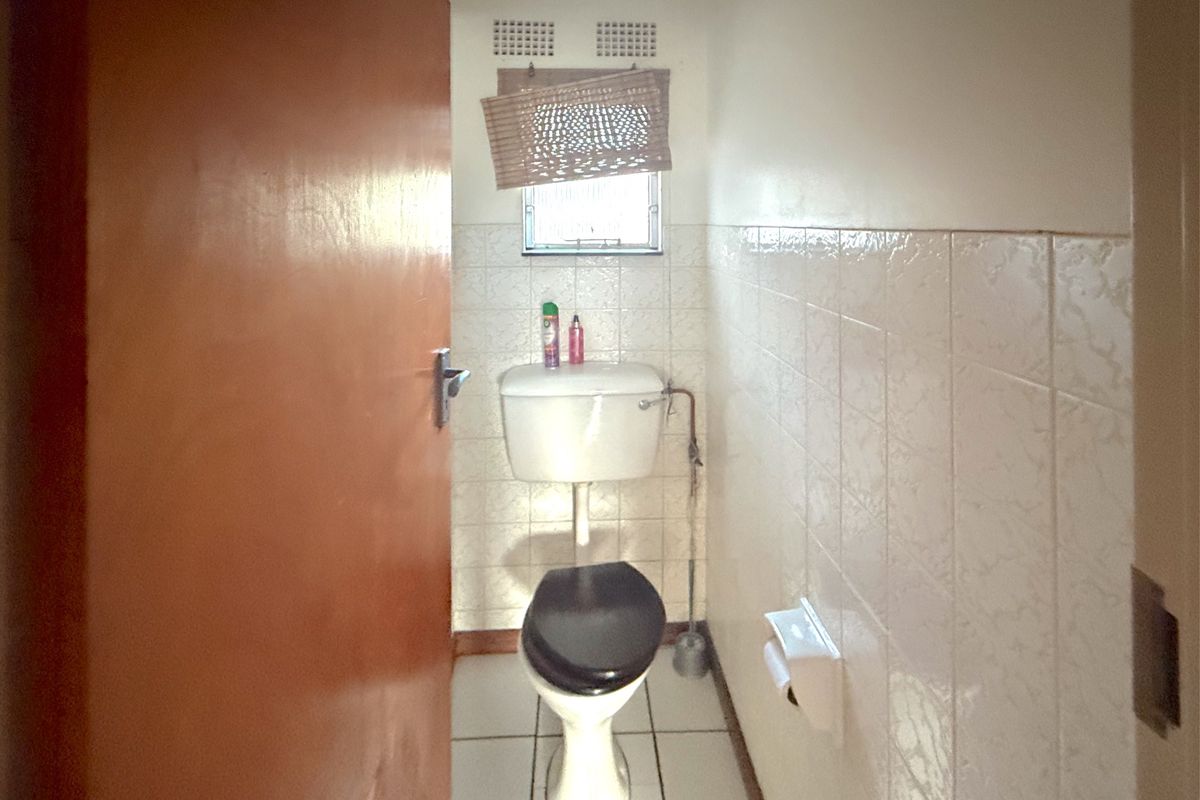 A compact, dated bathroom featuring ceramic wall and floor tiles, a standard toilet, and a small window with ventilation.