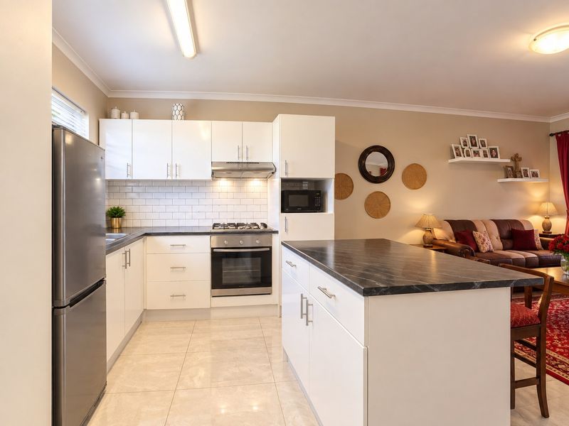 Modern open-plan kitchen featuring white cabinetry, subway tile backsplash, built-in oven, gas cooktop, and a functional kitchen island with stone-look countertops.
