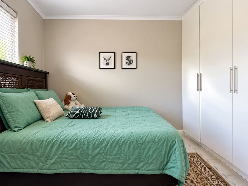 A well-maintained bedroom featuring neutral wall tones, tiled flooring, and a large built-in wardrobe with modern handles.