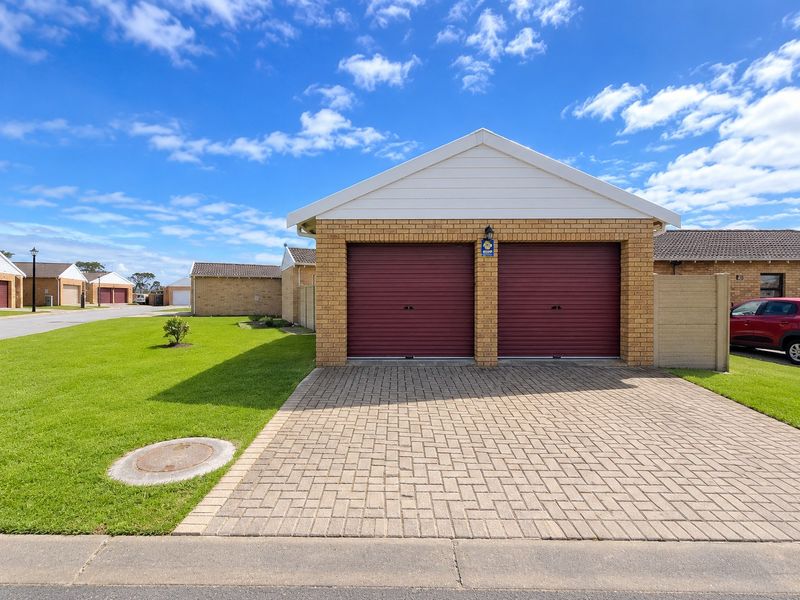 A well-maintained double garage with red roller doors, brick exterior, and a paved driveway in a residential townhouse complex.