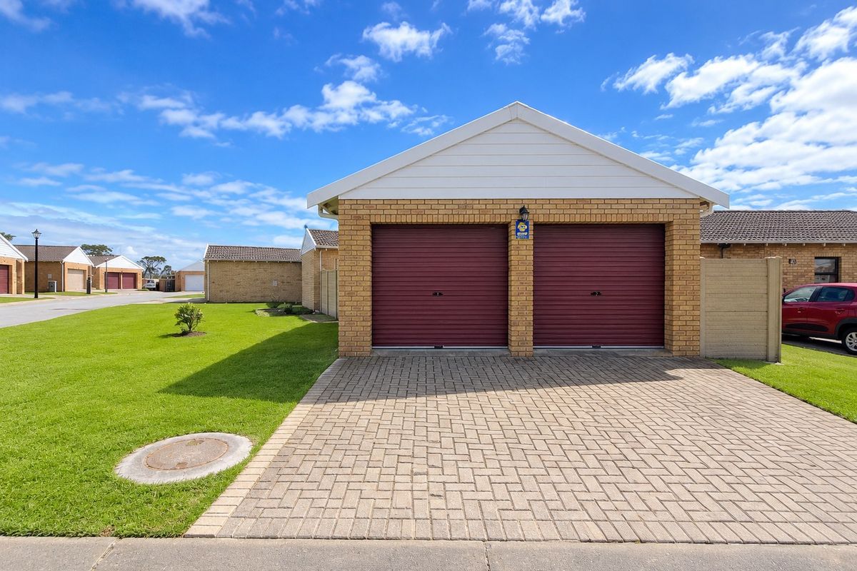 A well-maintained double garage with red roller doors, brick exterior, and a paved driveway in a residential townhouse complex.