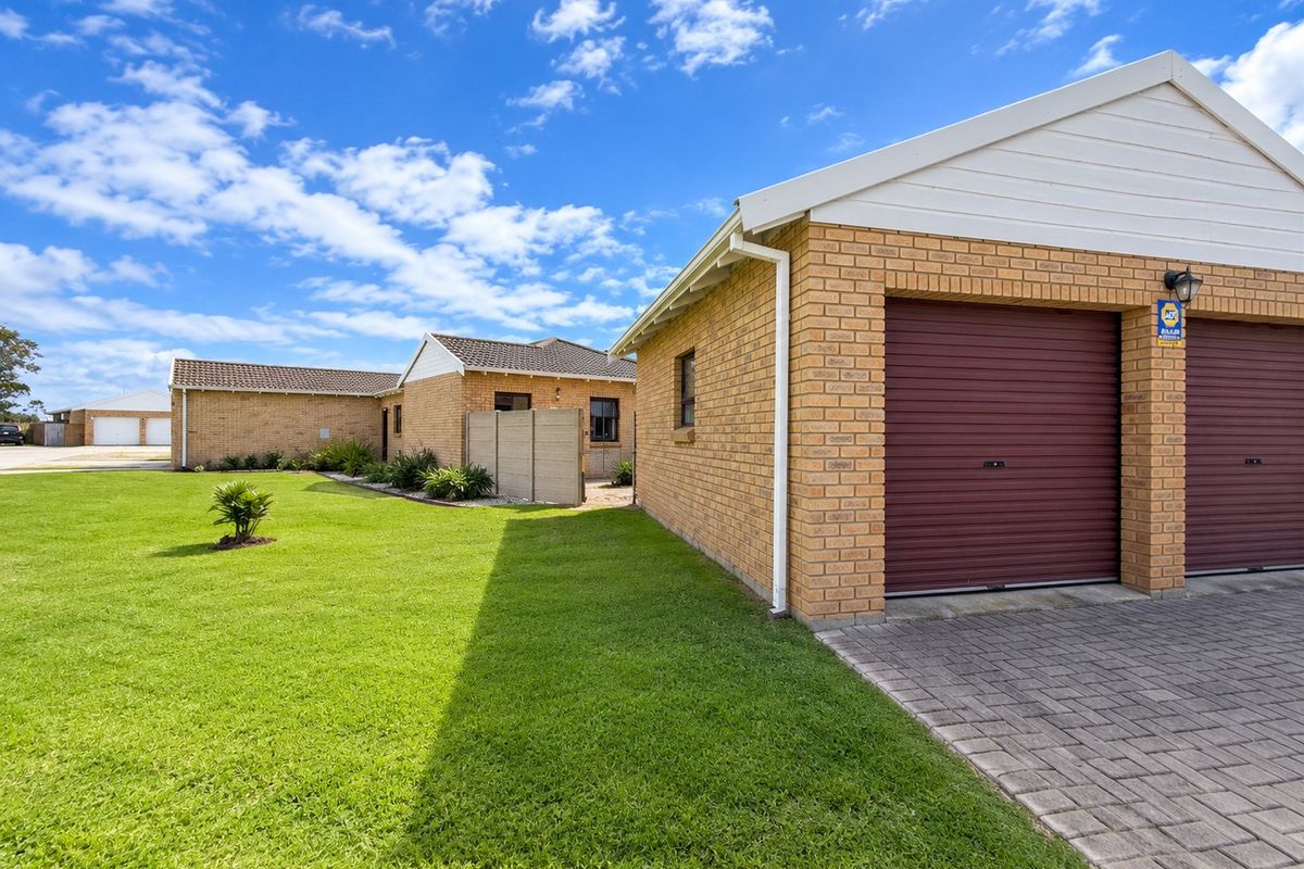 Exterior view of a brick townhouse featuring a double garage with a paved driveway and well-maintained lawn.