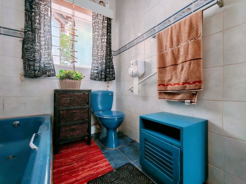 A dated bathroom featuring blue sanitaryware, ceramic wall and floor tiling, and a safety grab rail installed near the toilet.
