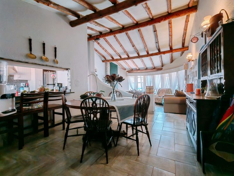 Spacious open-plan living and dining area featuring rustic exposed timber ceiling beams, tiled flooring, and a convenient pass-through window connecting to the kitchen.