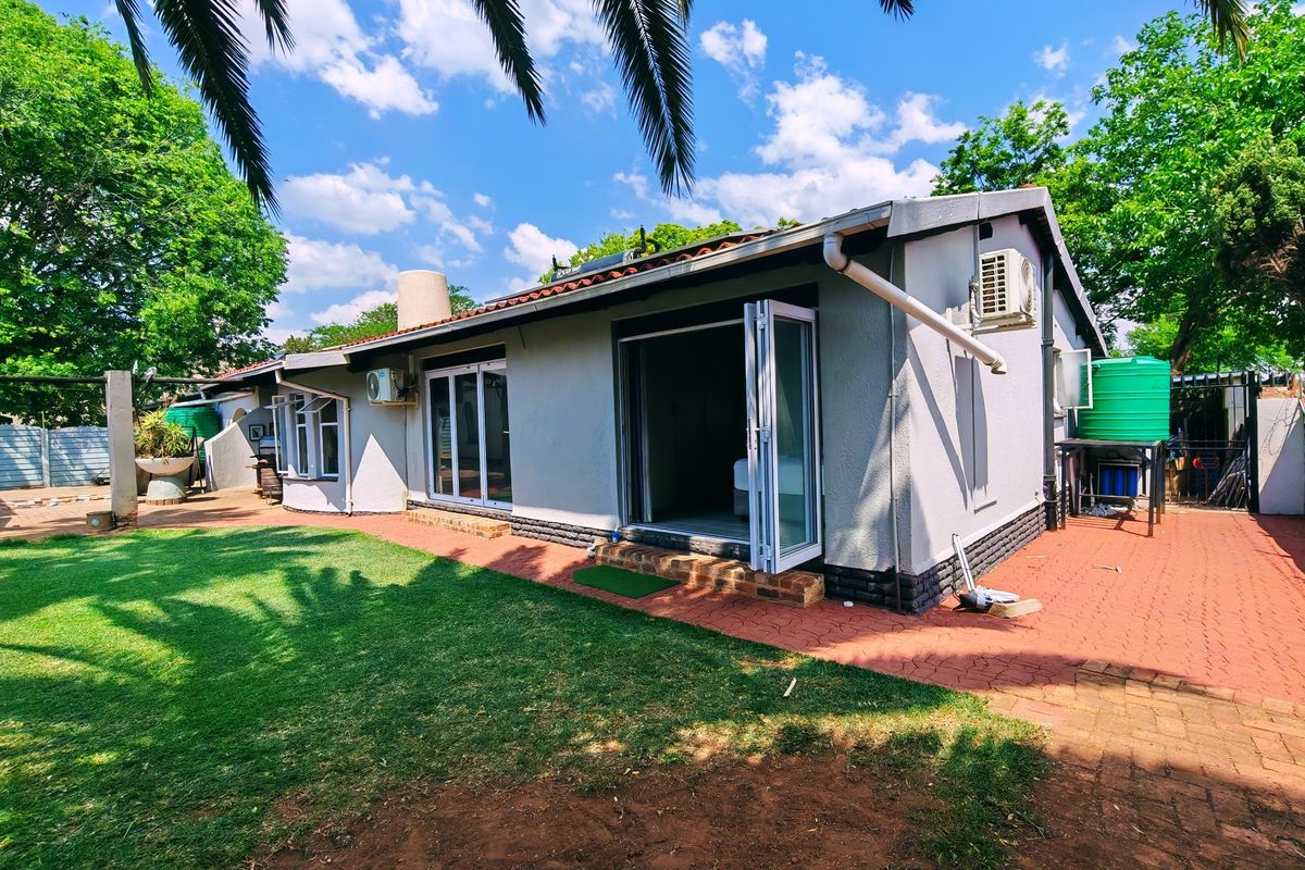 Rear view of the house featuring a paved patio area, bi-fold doors, and a water storage tank set within a landscaped garden.