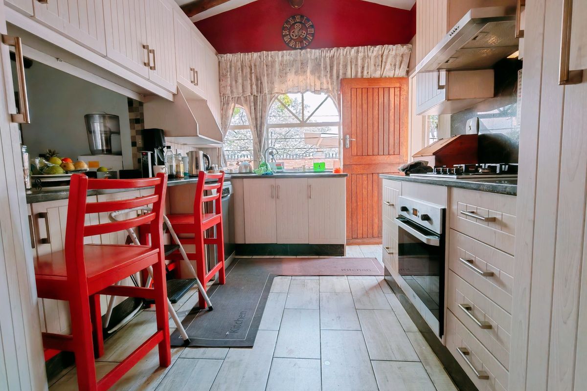 A functional kitchen featuring light-toned cabinetry, built-in oven and hob, tiled flooring, and exposed timber beams under a vaulted ceiling.