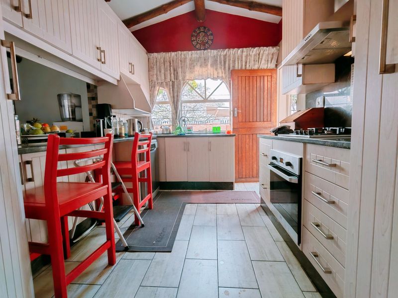 A functional kitchen featuring light-toned cabinetry, built-in oven and hob, tiled flooring, and exposed timber beams under a vaulted ceiling.