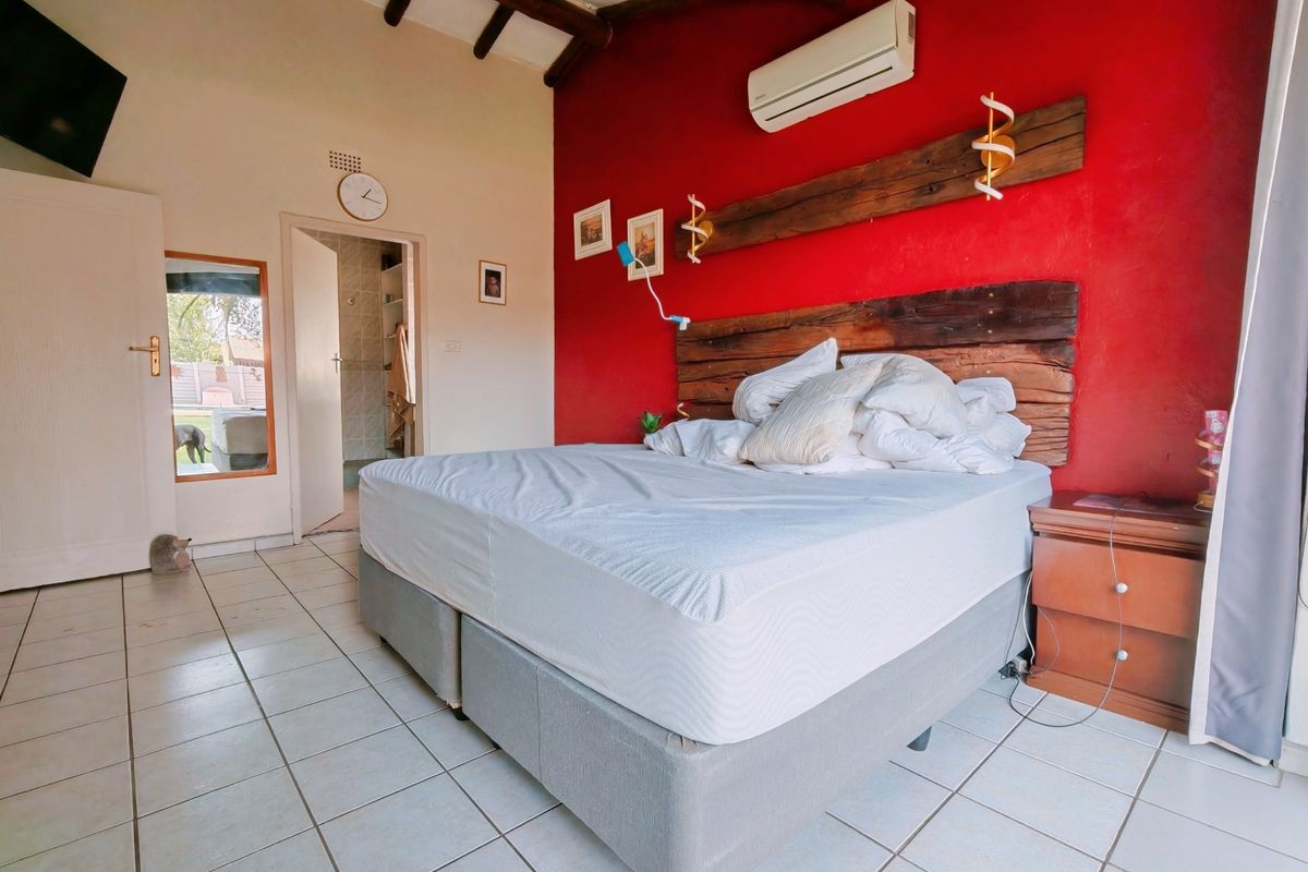 Bedroom featuring exposed timber ceiling beams, tiled flooring, a split-system air conditioner, and a built-in timber headboard feature against a red accent wall.