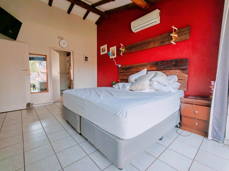 Bedroom featuring exposed timber ceiling beams, tiled flooring, a split-system air conditioner, and a built-in timber headboard feature against a red accent wall.
