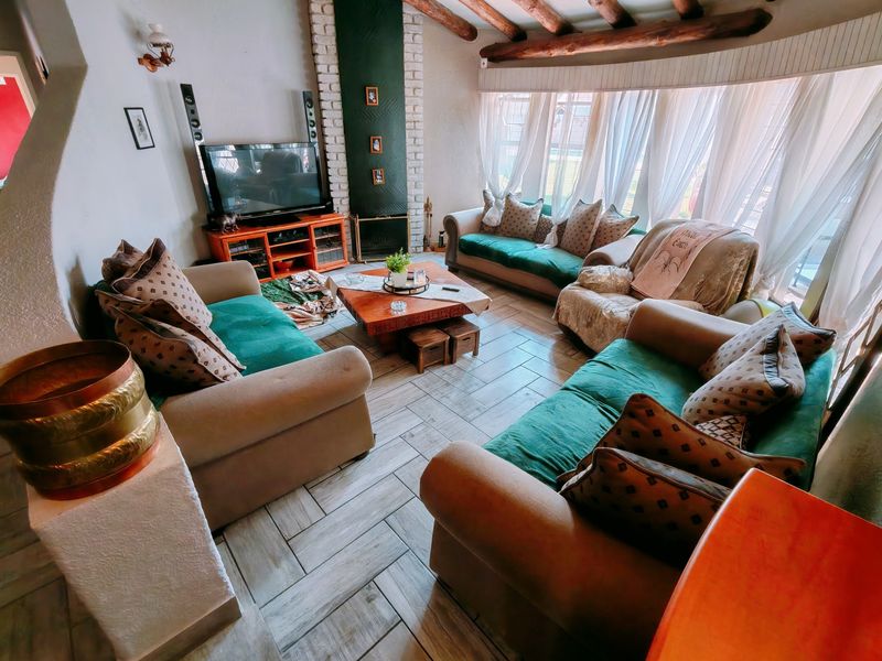 A cozy living room featuring exposed timber ceiling beams, a brick fireplace surround, and large windows that provide ample natural light.