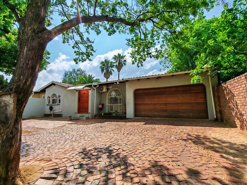 Front elevation of the property featuring a cobblestone driveway, wooden garage door, and a secure entrance with a wooden front door.