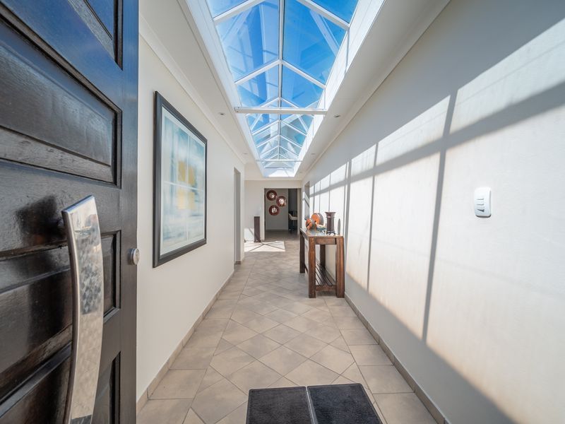 A bright and spacious entrance hallway featuring a large glass skylight, tiled flooring, and a modern solid wood front door.