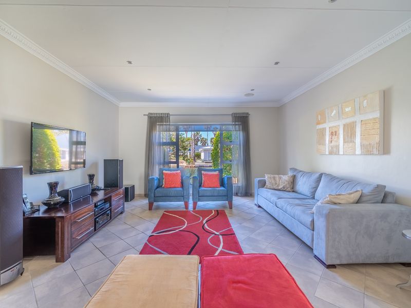 A well-maintained living room featuring tiled flooring, recessed downlighting, decorative ceiling cornicing, and a large window providing natural light.