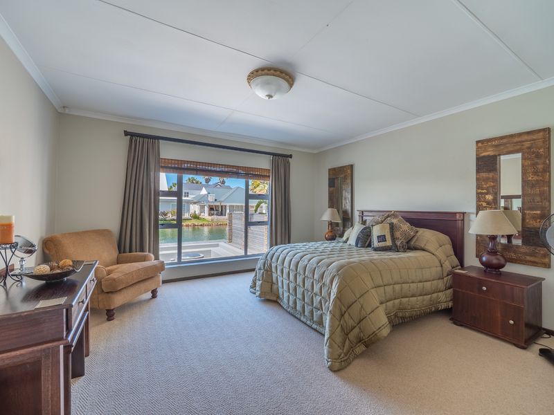 A spacious bedroom featuring neutral carpeting, a large window with views of the canal, and a central ceiling light fixture.