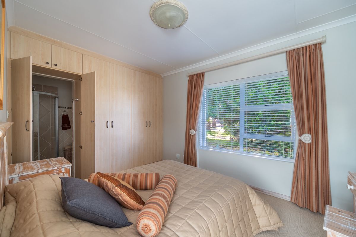 A well-lit bedroom featuring built-in wooden cupboards, neutral carpeting, and direct access to an en-suite bathroom.
