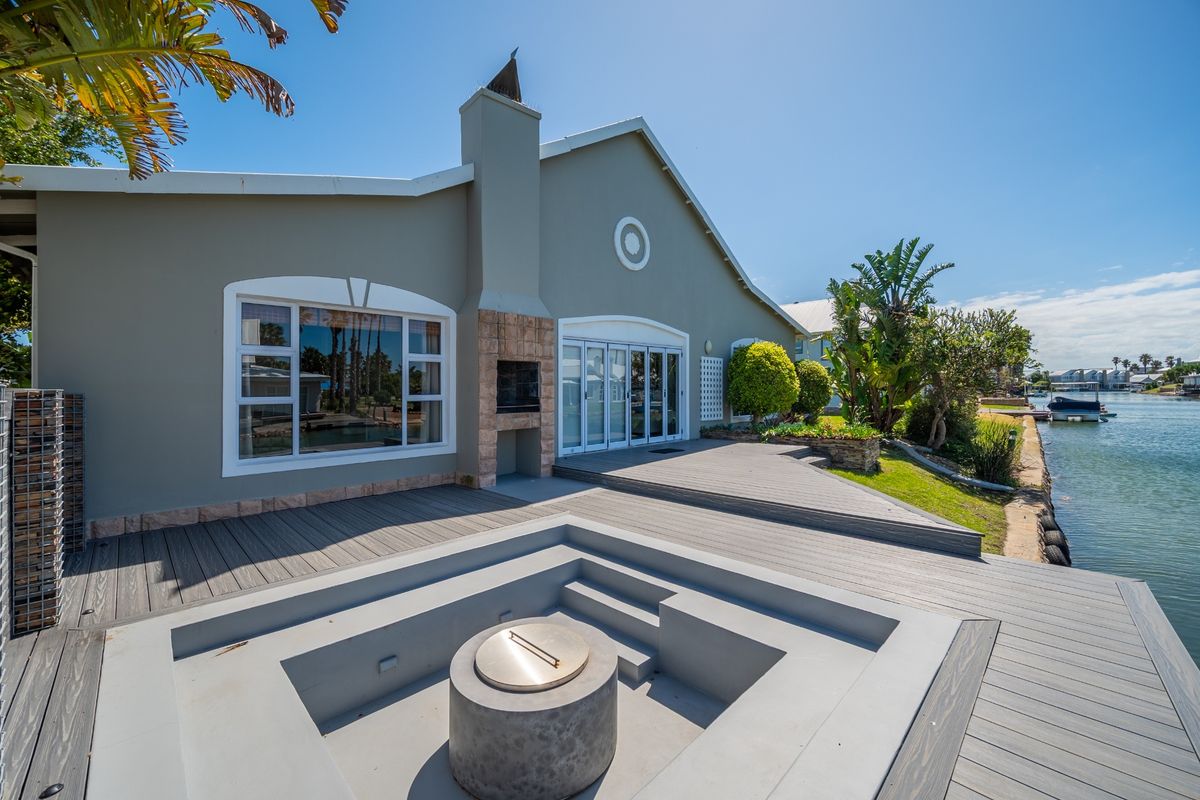 Rear exterior view featuring a modern sunken fire pit, composite decking, built-in fireplace, and direct access to the waterfront.